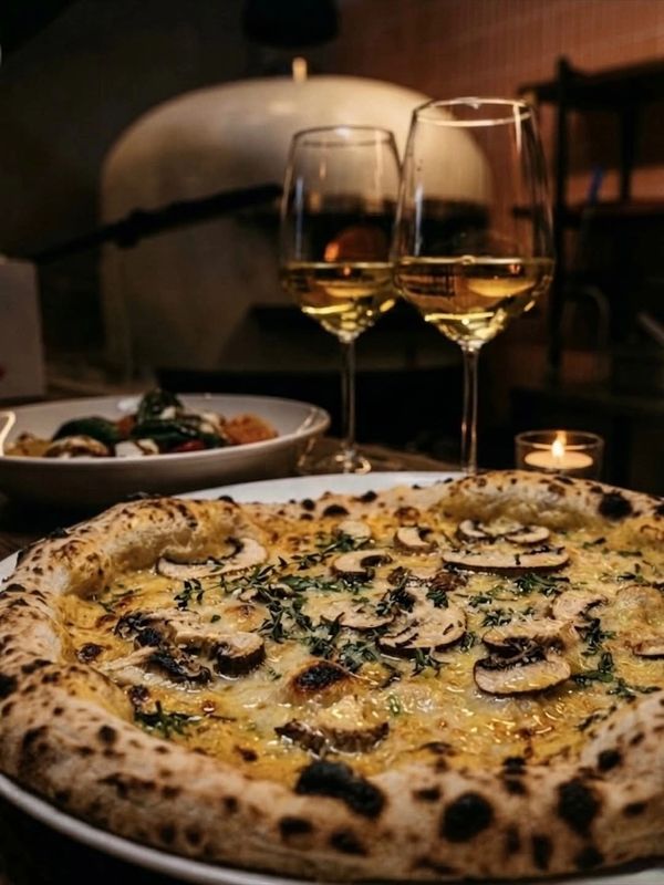 Gourmet mushroom pizza with two glasses of white wine in a cozy setting.
