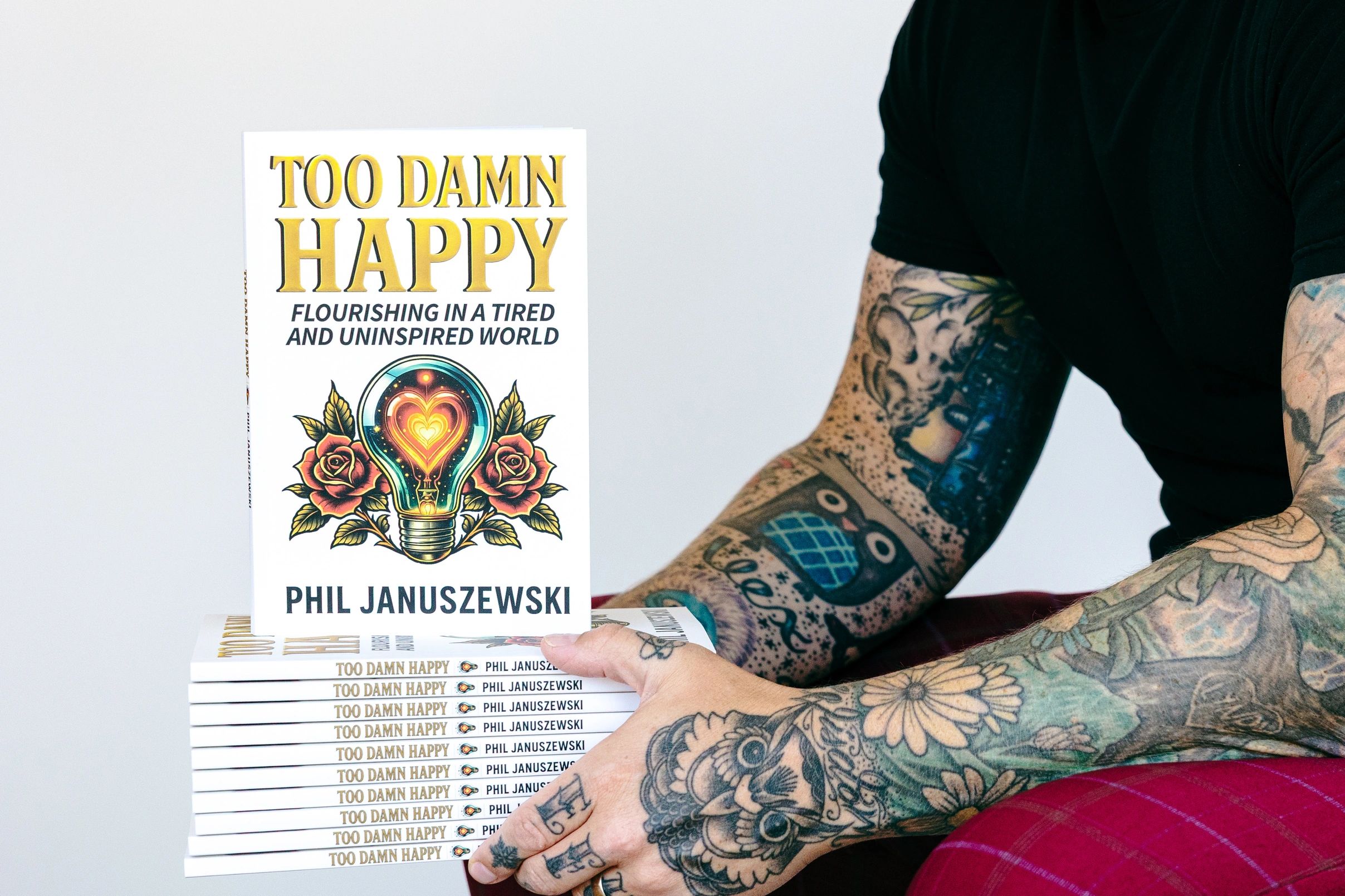 Stacked copies of Too Damn Happy by author and keynote speaker Phil Januszewski, a personal developm