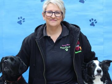 Woman with glasses posing with two dogs against a blue backdrop with paw prints.