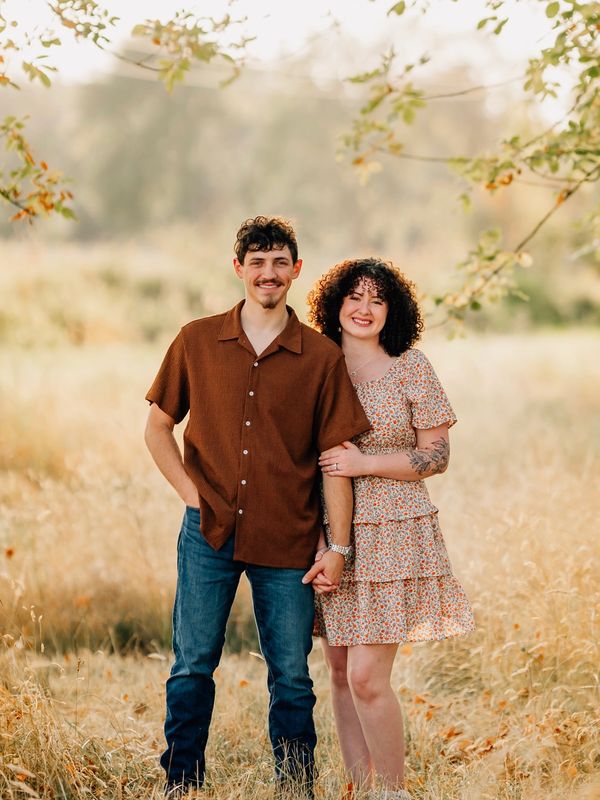 Smiling couple holding hands in a sunlit field during golden hour.