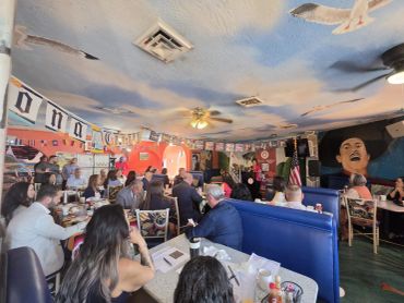 Crowded restaurant with mural and ceiling art.