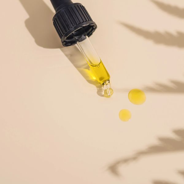 A CBD oil tincture dropper with two drops of hemp oil and the shadow of a hemp plant to the right