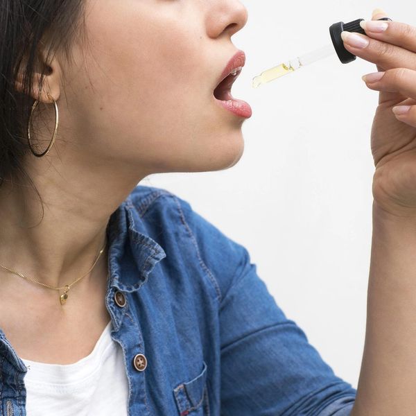 A woman holding a tincture dropper and getting ready to take a serving of CBD