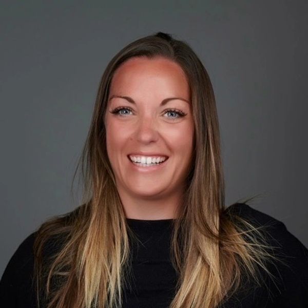 Smiling woman with long blonde hair against a gray background.