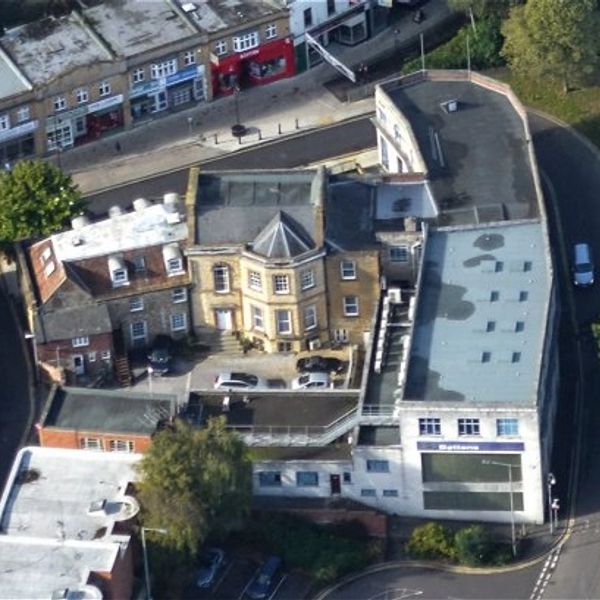Aerial view of a mixed-use building with cars parked outside and shops nearby.