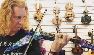 man with long hair playing an electric violin in front of violins
