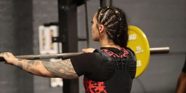 Woman lifting weights with braided hair and tattoos.