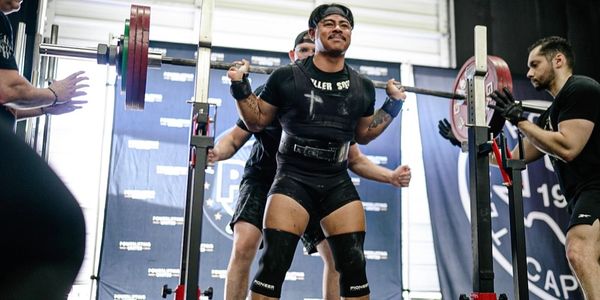 Man powerlifting with spotters in a gym.