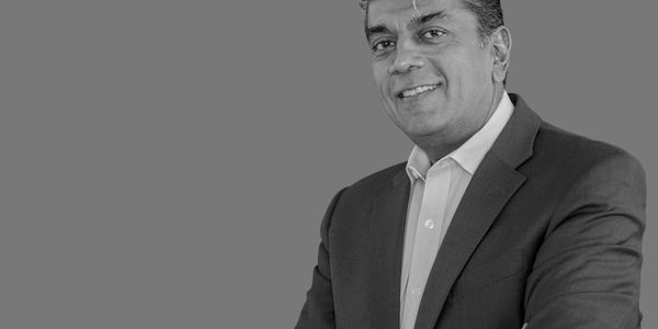 Smiling man in a suit with arms crossed and pen in hand.