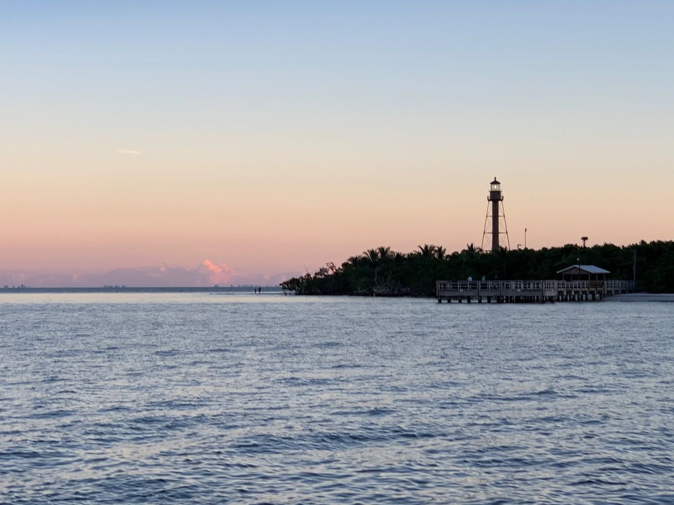 Lighthouse on a small island at sunset with calm waters.