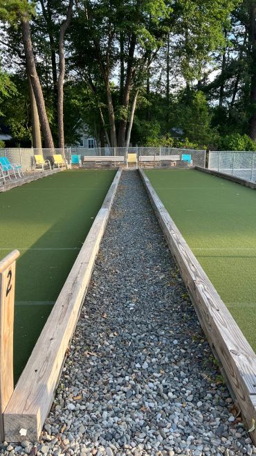 Outdoor bocce ball courts surrounded by trees and chairs.