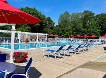 Empty poolside chairs and red umbrellas on a sunny day.