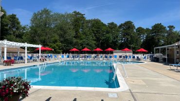 Outdoor swimming pool with red umbrellas and lounge chairs.