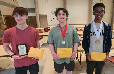 Three young men holding awards and envelopes, smiling in a room.
