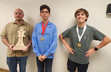 Three young men stand proudly with medals and a trophy for a competition win.