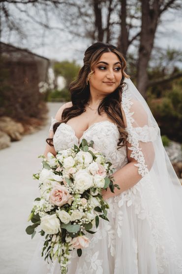 Bride in elegant lace wedding dress holding a cascading bouquet.
