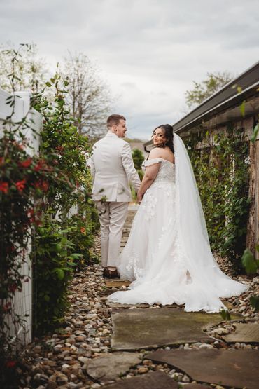 Bride and groom walking hand in hand down a garden path on their wedding day.