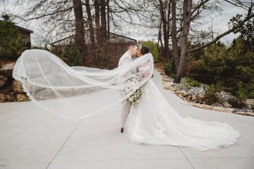 Bride and groom kissing outdoors with bride's veil flowing.