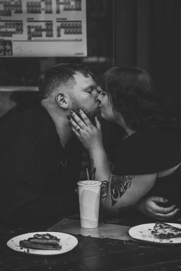 A couple shares a tender kiss at a table with food and drinks.
