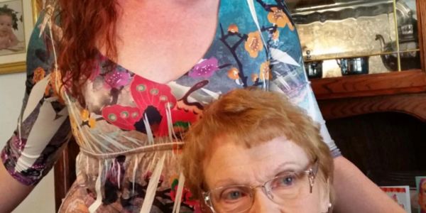 Two women smiling indoors with a colorful dress and glasses.