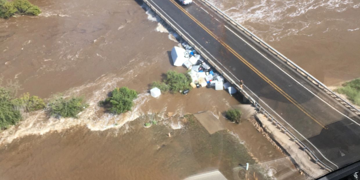 Floodwaters surround a bridge with debris caught at the edge.