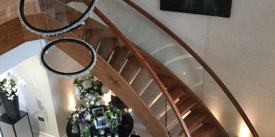 Elegant wooden spiral staircase with glass railing in a modern home.