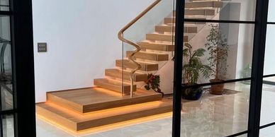 Modern wooden staircase with LED lighting and potted plants in a bright room.