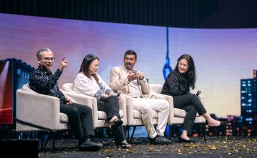 Four people engaged in a panel discussion on stage with a cityscape backdrop.