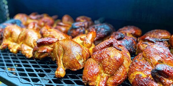 Whole chickens being smoked on a grill with a rich golden-brown color.
