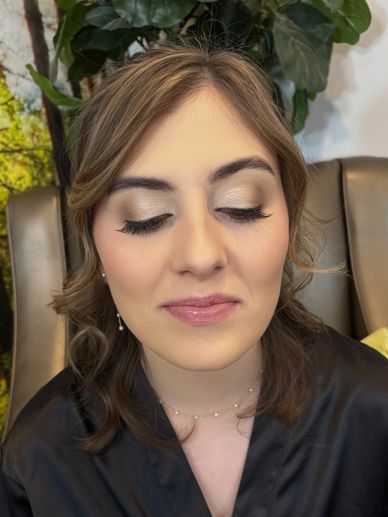 Woman with elegant makeup and closed eyes, sitting in a cozy setting.