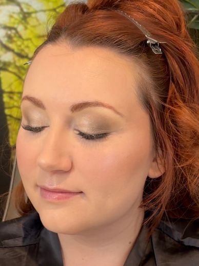 Woman with closed eyes showing natural makeup and red hair clipped back.