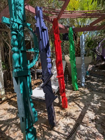 Colorful wooden sculptures hanging outdoors in sunlight.