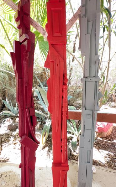 Three tall wooden sculptures painted red, burgundy, and gray.