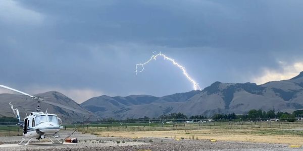 Helicopter on the ground with lightning striking the mountain in the background.