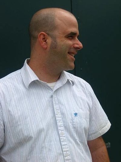 Profile of a smiling bald man against a dark background.