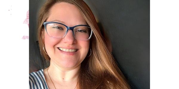 Smiling woman with glasses and long hair against a dark background.