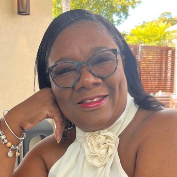 Smiling woman wearing glasses and a white top with a flower detail.