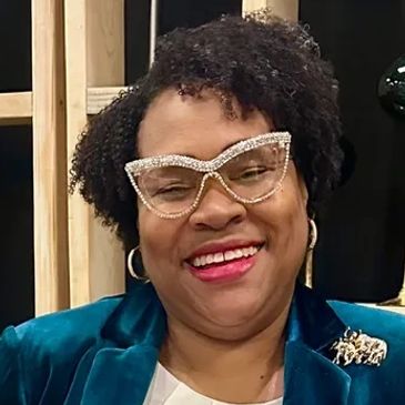 Smiling woman wearing unique rhinestone glasses and a teal blazer.