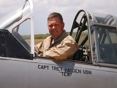 A man in a military flight suit sits in an aircraft cockpit.