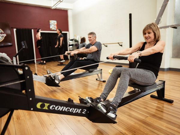 Two older adults exercising on rowing machines in a gym.