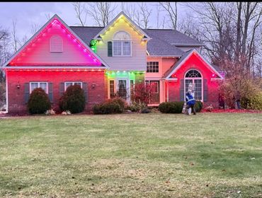 A house decorated with colorful Christmas lights and a person carrying a ladder.