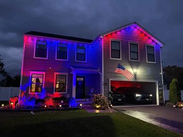 House lit with red, white, and blue lights at night, displaying an American flag.
