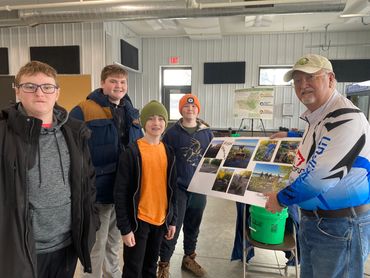 A group of boys and an older man holding a collage poster indoors.