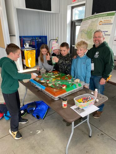 Children and an adult engage with an interactive watershed model indoors.
