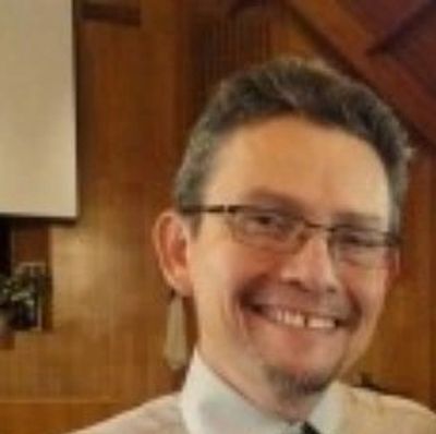 Smiling man with glasses in a wood-paneled room.