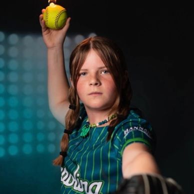 Young girl in softball uniform preparing to pitch a ball.
