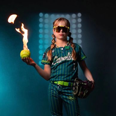 Young softball player holding a flaming ball, looking confident in uniform.