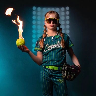 Young softball player holding a flaming ball, looking confident in uniform.
