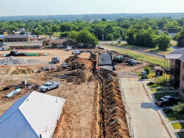 Aerial view of construction site with trenching, equipment, and newly paved road section.