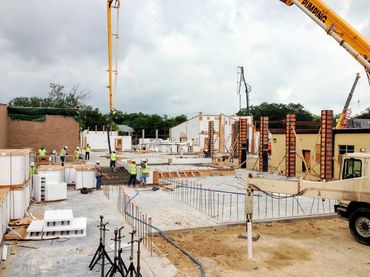 Active construction site with workers, cranes, concrete forms, and building materials under cloudy s